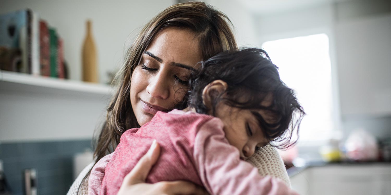 Portrait of mother holding sleeping baby in kitchen