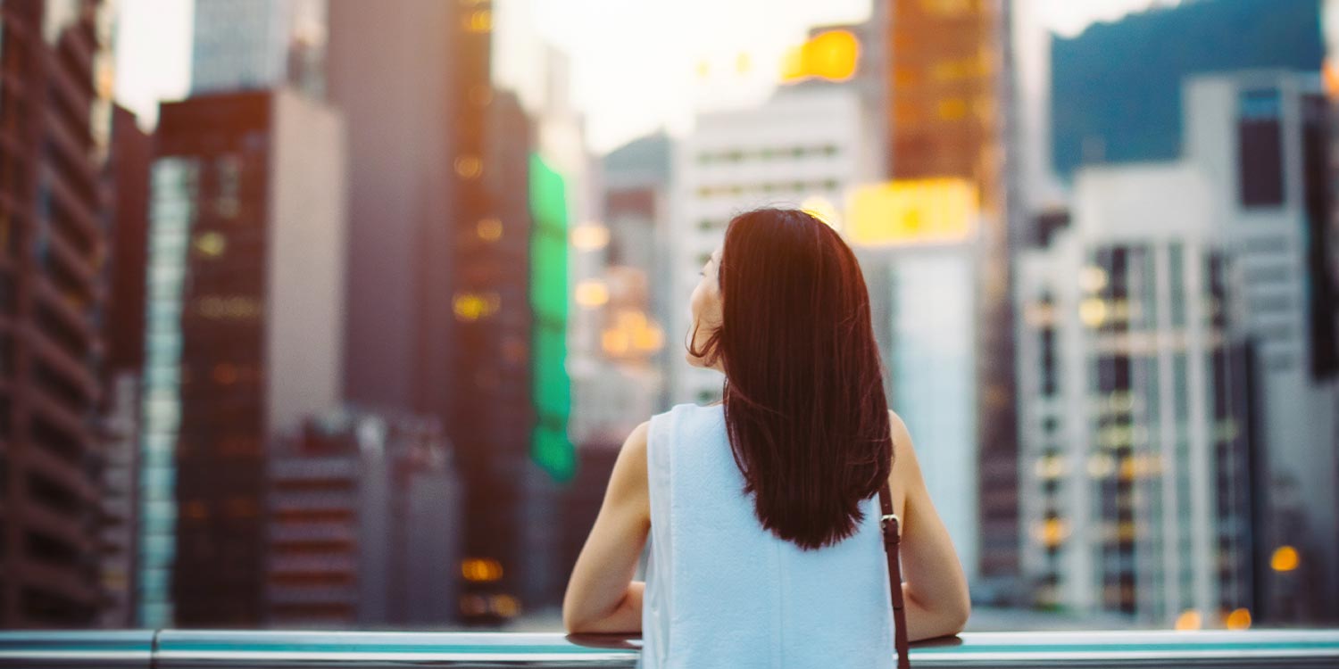 Rear view of woman looking up to sky with smile on a fresh bright morning in city