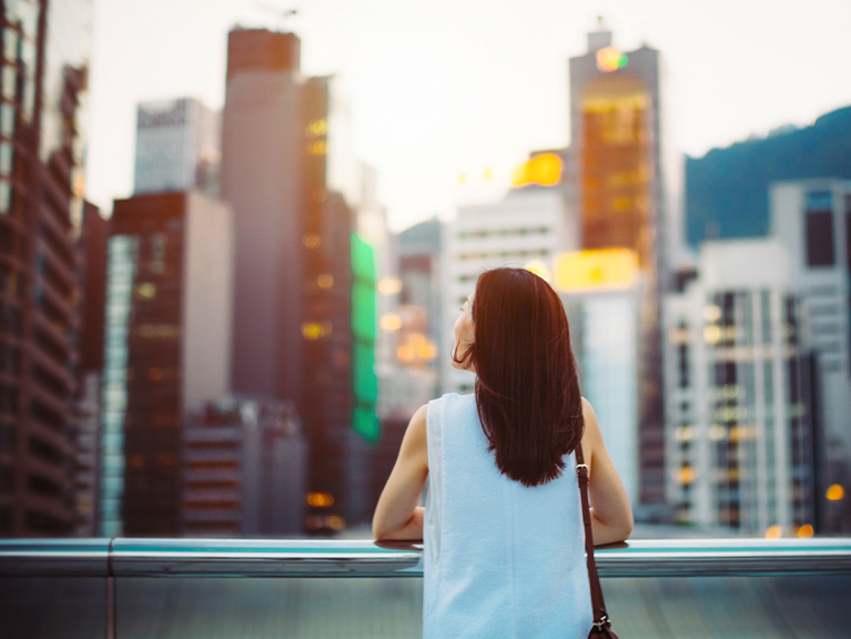 Rear view of woman looking up to sky with smile on a fresh bright morning in city